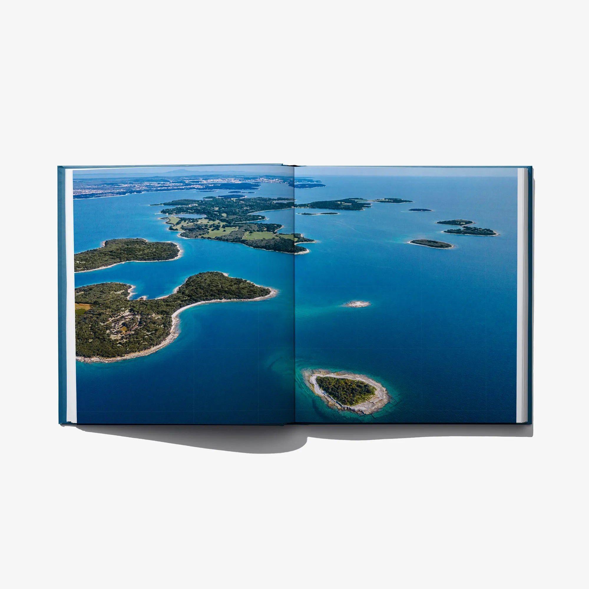 Open photo book spread with aerial view of islands and turquoise water.