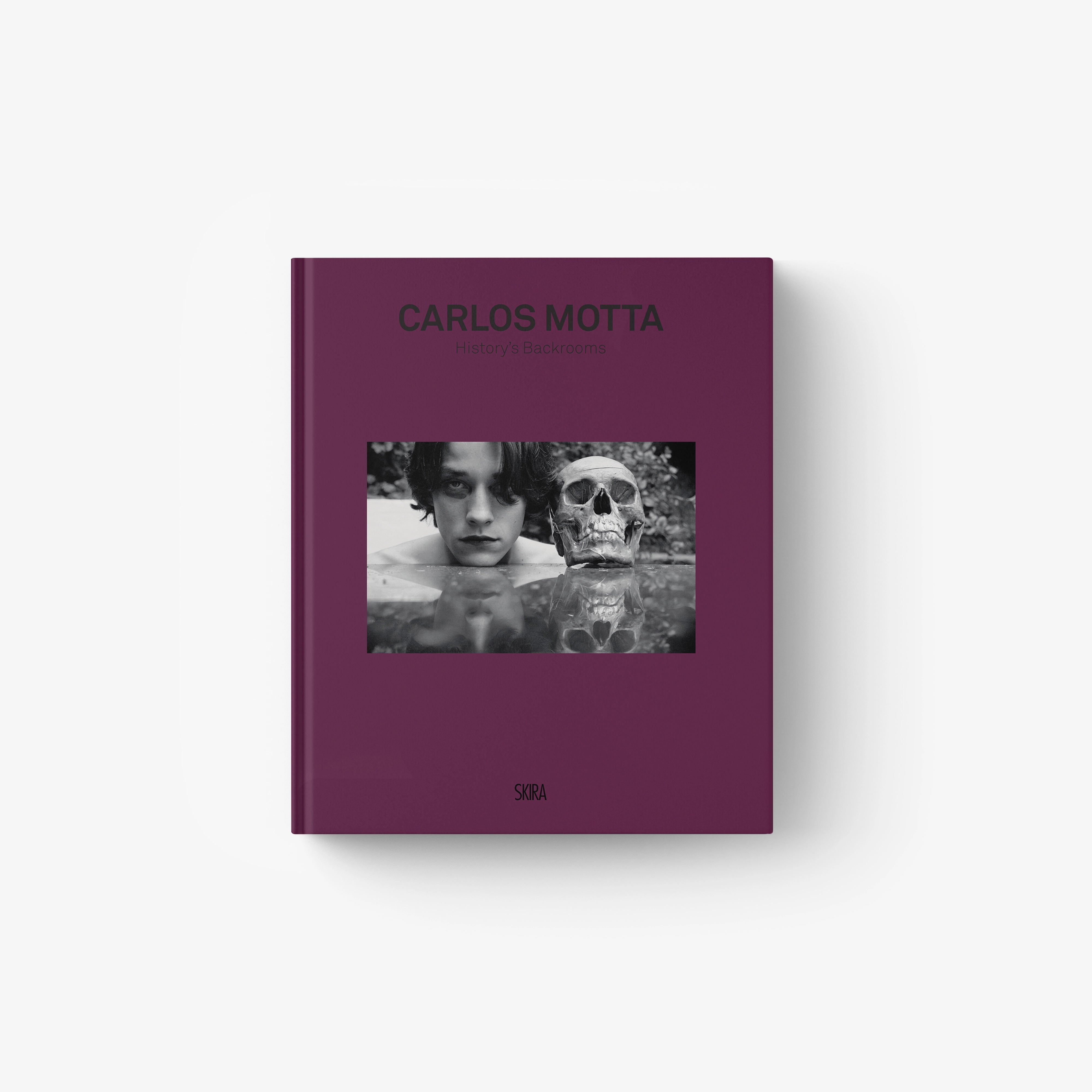 Deep purple hardcover book titled "Carlos Motta" with black-and-white photo of a man and a skull on the cover.