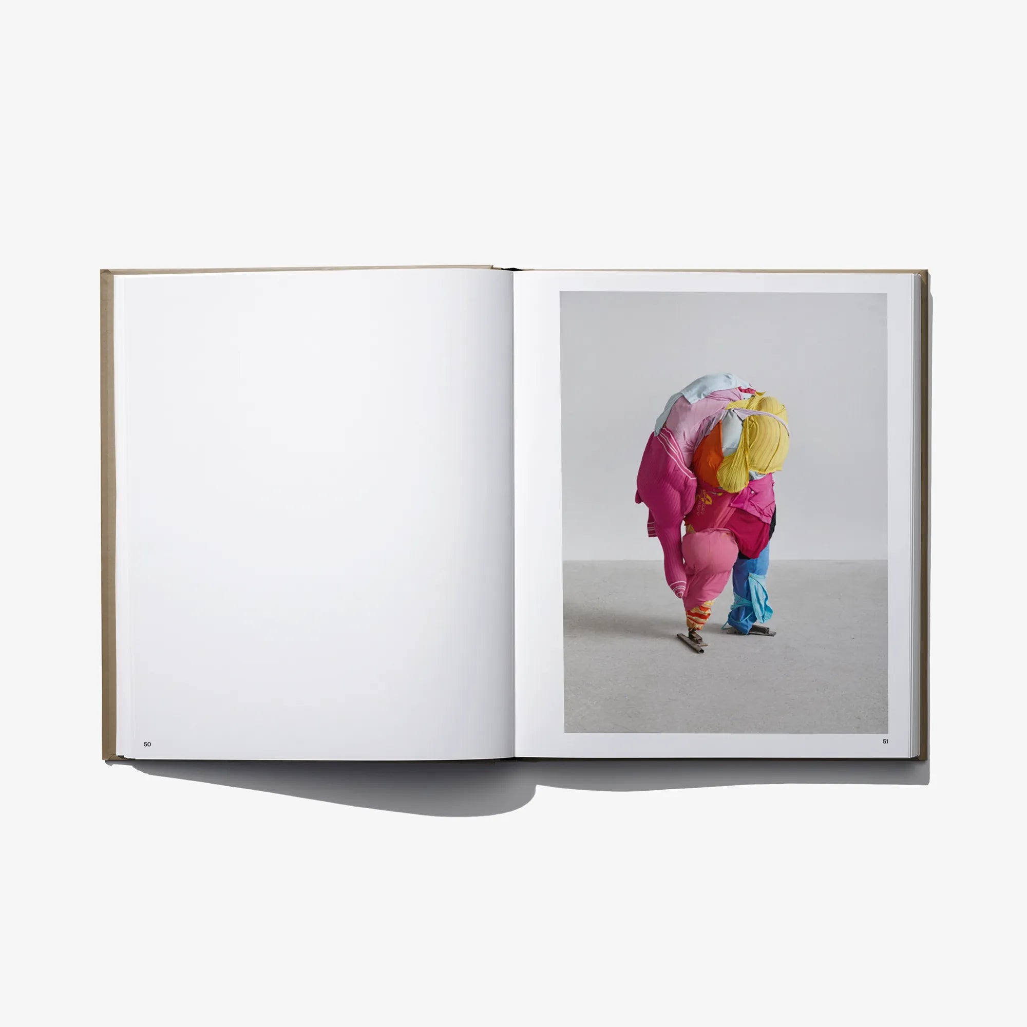 Open art book with blank left page and colorful kneeling sculptural figure on right.