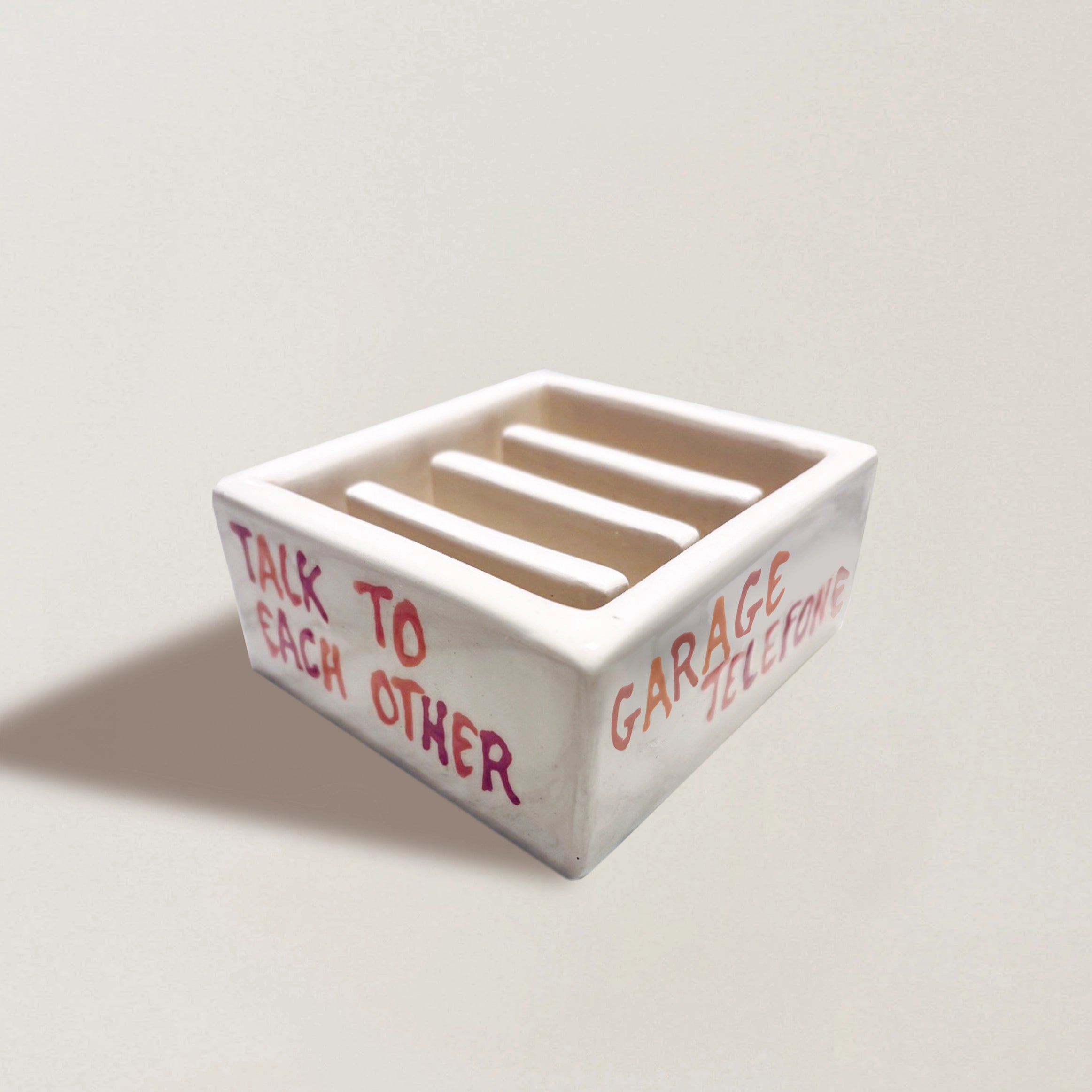 Handmade white ceramic phone stand with slot rails and red 'TALK TO EACH OTHER' text.