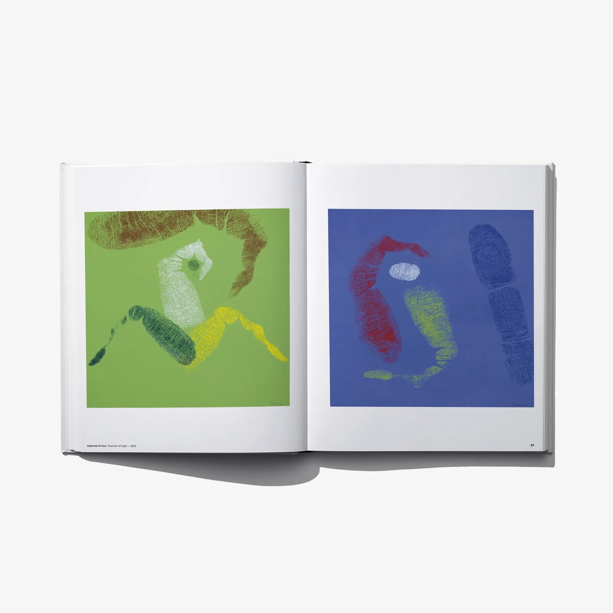 Open art book spread with two square prints on green and blue backgrounds