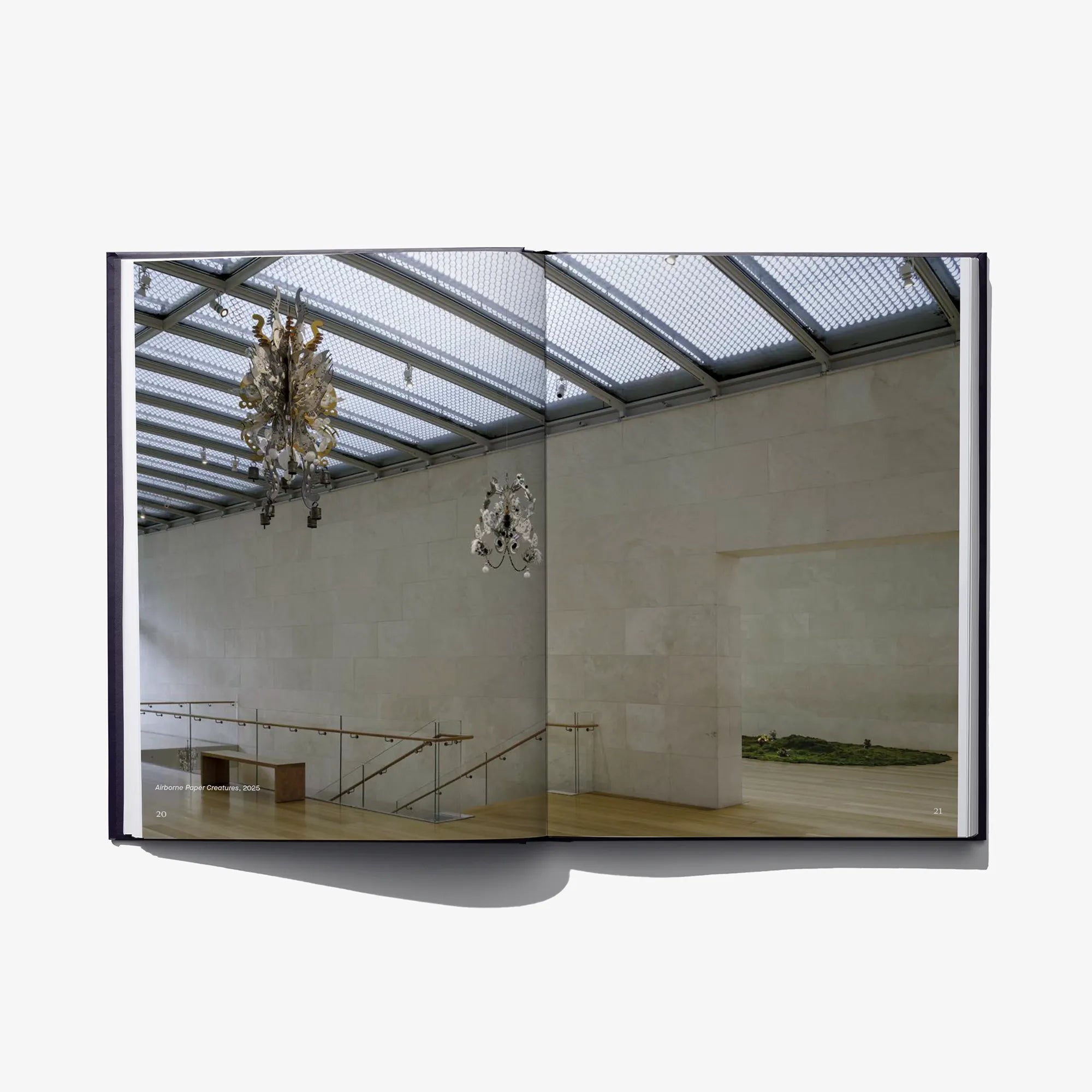 Open hardcover art book showing gallery photo with hanging chandelier-like sculptures