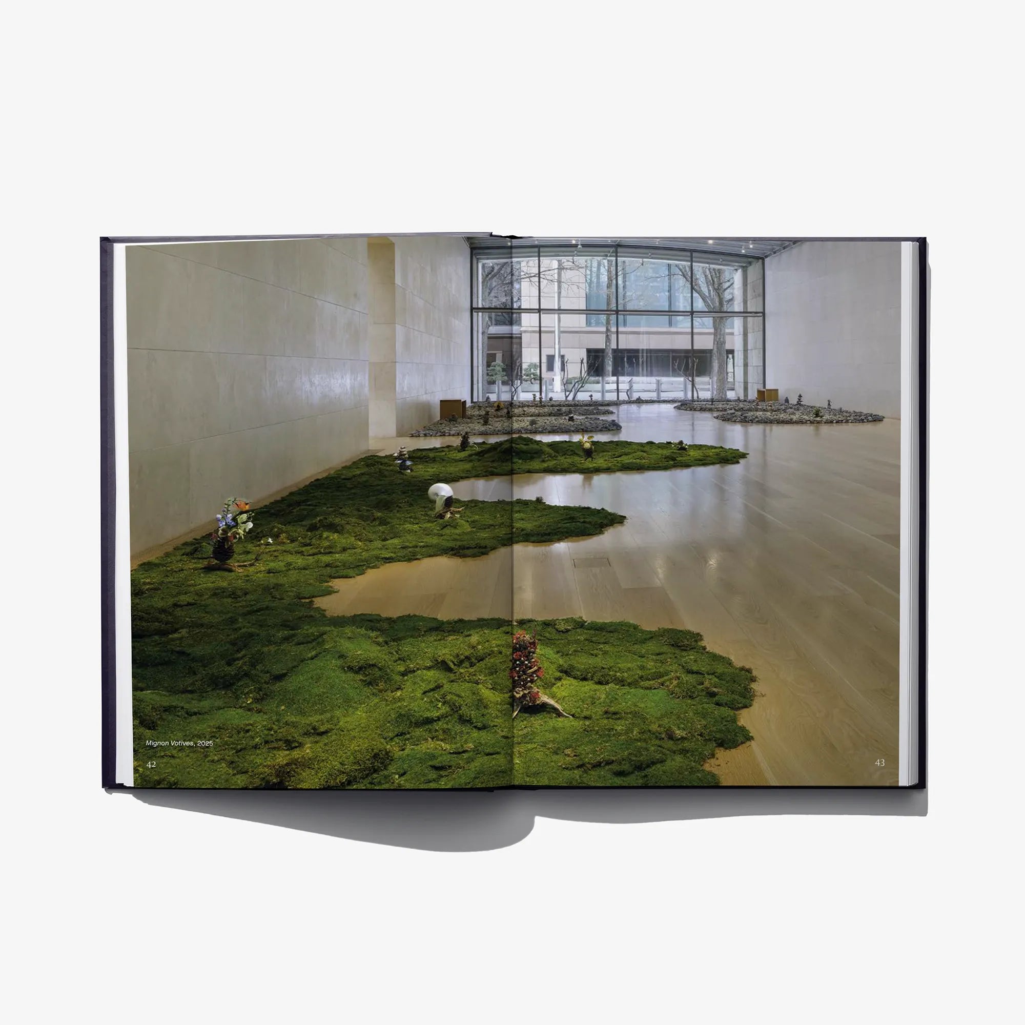 Open hardcover art book with gallery photo of moss-covered floor islands and windows