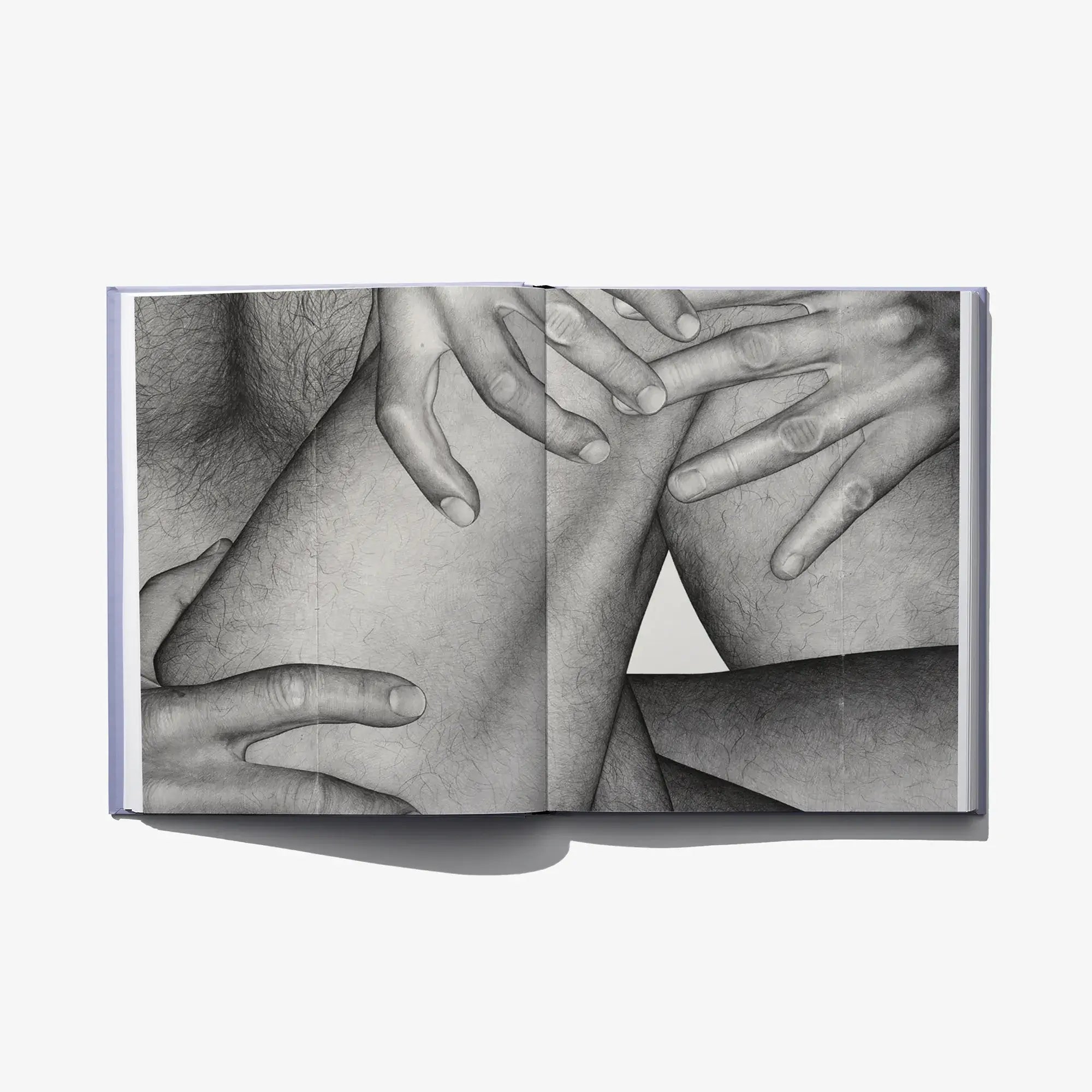Open art book spread showing black-and-white torso and interlaced hands