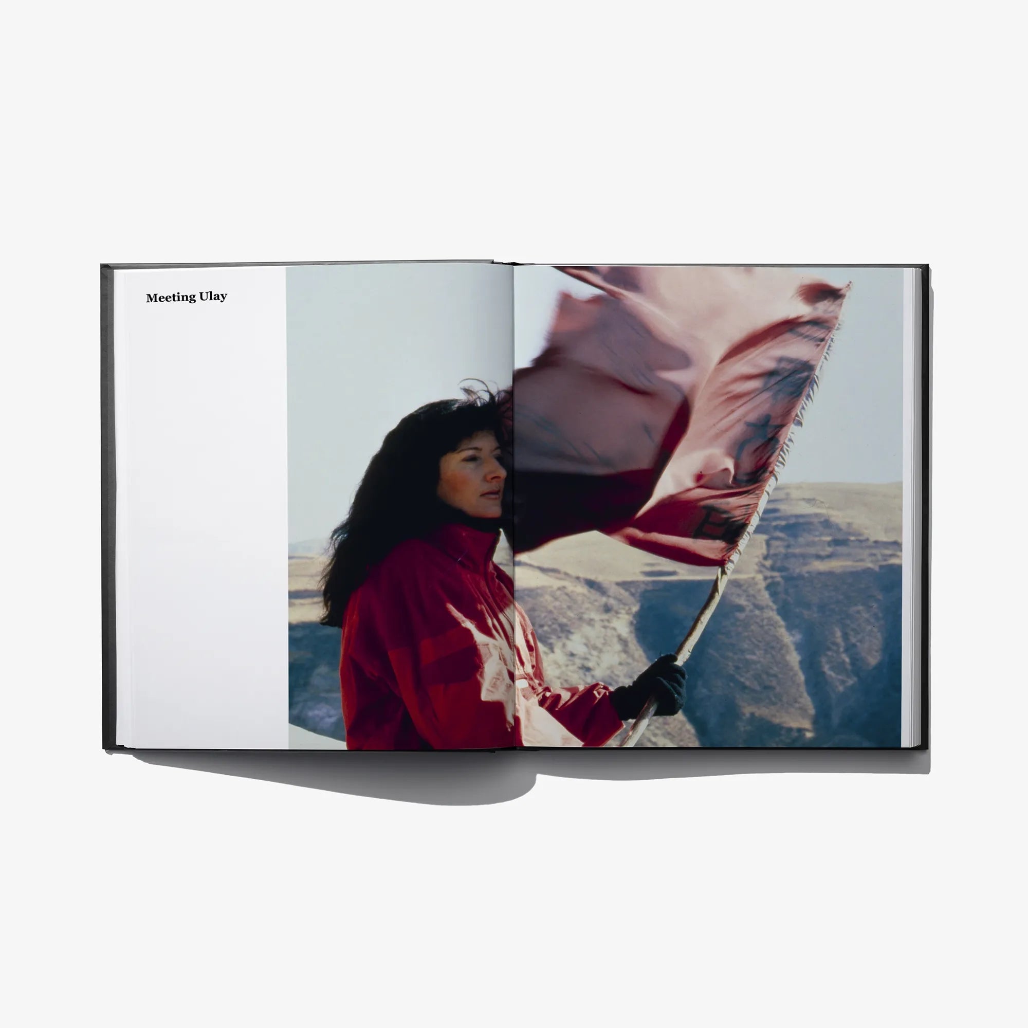 Open photo book spread with a person in red holding a large flag outdoors.