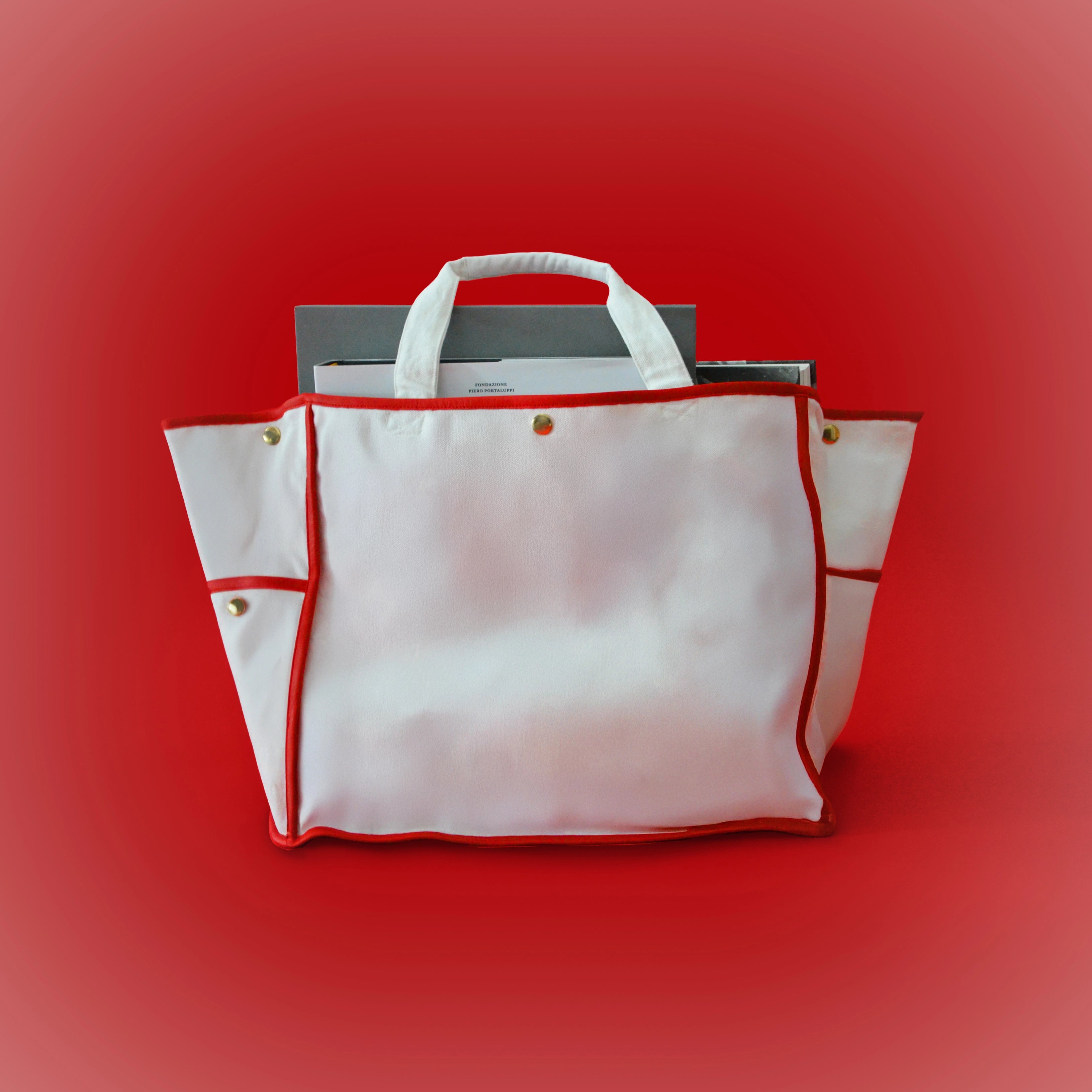 White canvas tote bag with red trim, top handles, and gold hardware