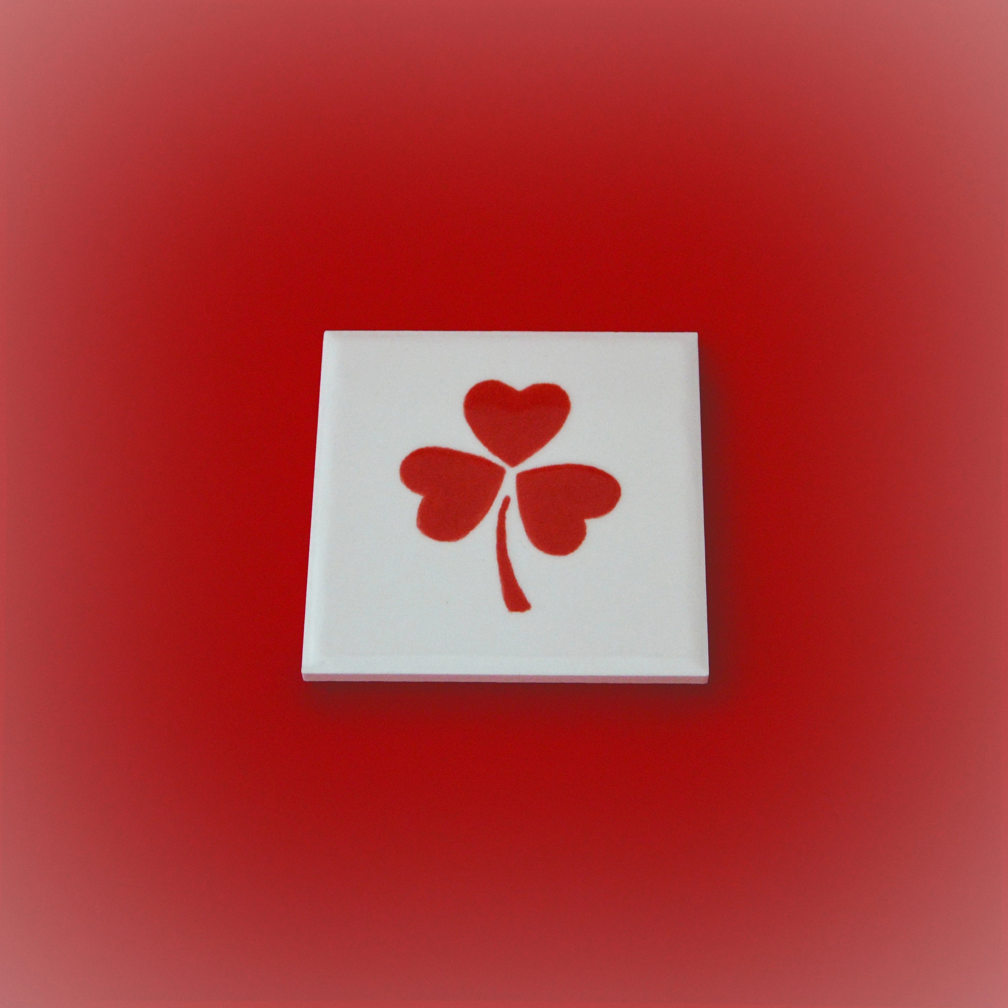 Square ceramic tile with white base and red four-petal heart clover design