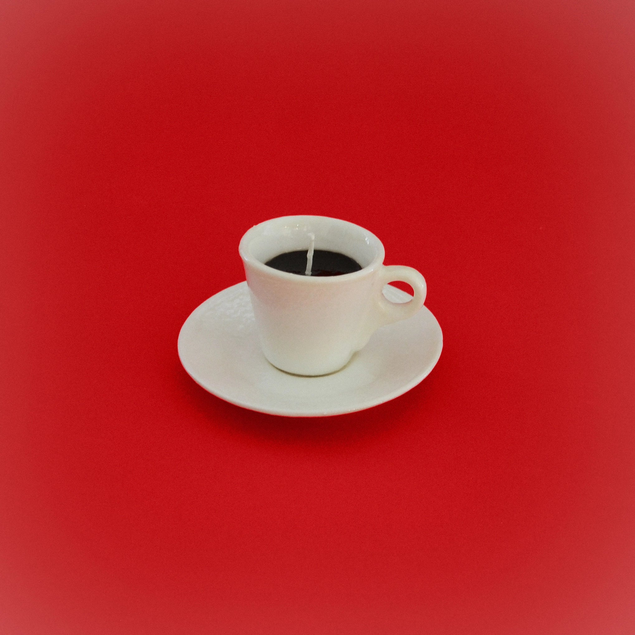 White coffee cup candle with black wick in ceramic cup and matching saucer