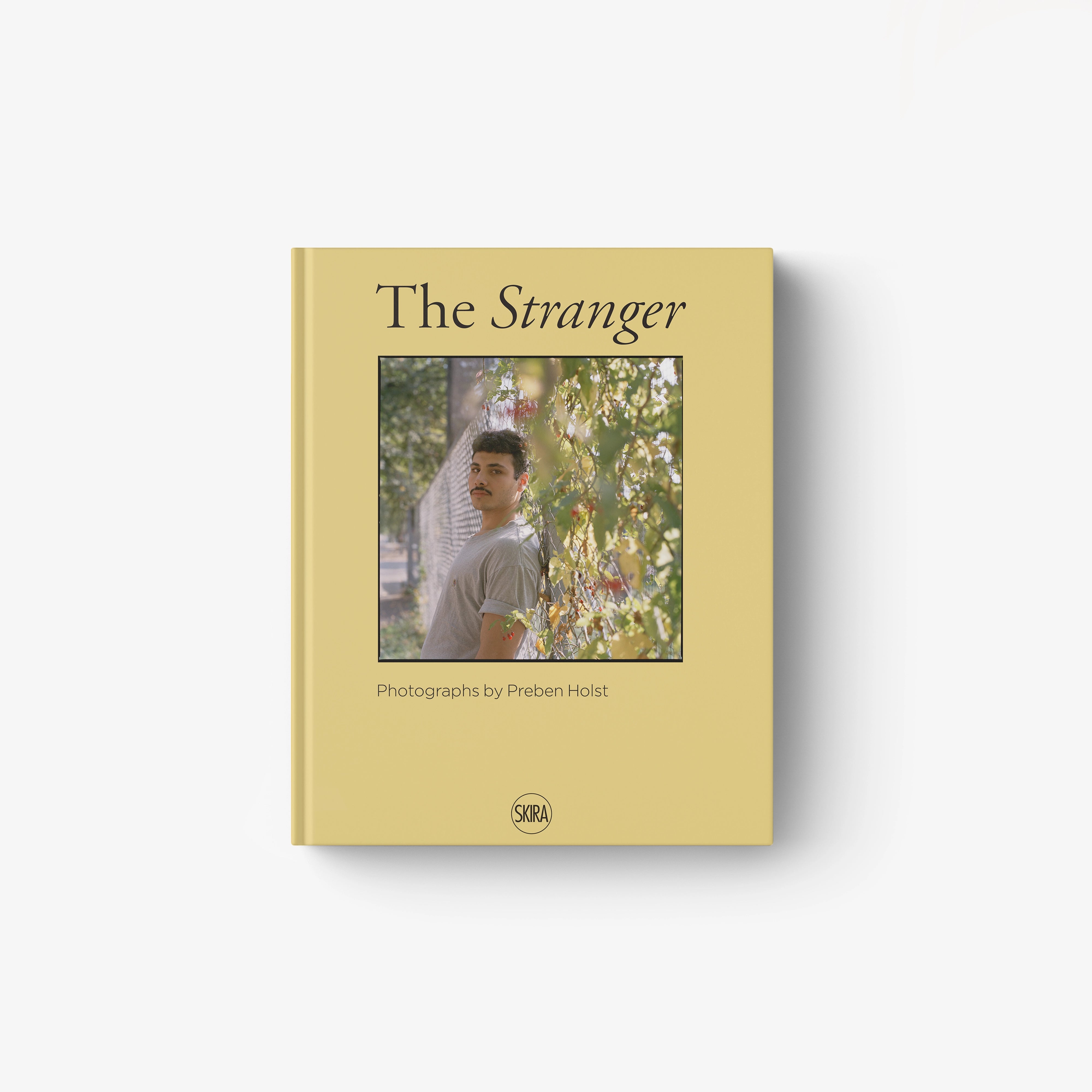 Soft mustard yellow book cover titled The Stranger with a color portrait of a man amidst foliage.